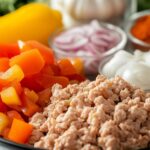 Close-up of fresh ingredients for ground chicken chili, including ground chicken, diced bell peppers, onions, garlic, and spices on a kitchen counter